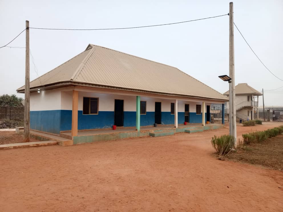 A classroom block at Crown Crest Academy, white and blue with a wide veranda, seen from the sandy compound.