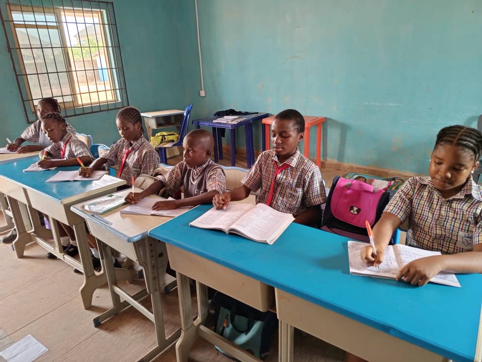 Pupils writing in exercise books, with open textbooks on the desks between them.